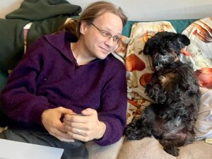 Me and Kifl sit on the sofa; Kifl, a terrier, is ridiculous. She is sitting like an alert bunny, while I gaze at her in amusement.