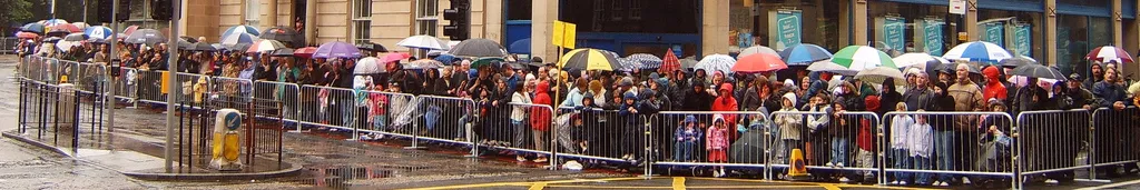 For illustration: Many people standing around behind barriers, getting rained on.