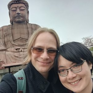 A giant Buddha leans over the author and their partner, who look happy.