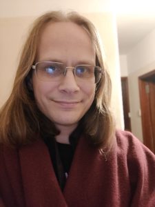 A portrait of the author: a white person of indeterminate age (actually 46), with shoulder-length brown-blonde hair and a burgundy shawl.